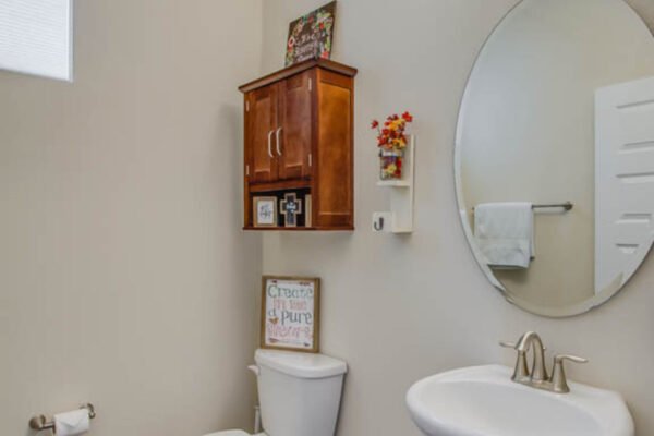Modern bathroom with a round mirror, wooden cabinet, decorative wall art, and a white sink and toilet, showcasing stylish features in a home for sale in Winter Garden, FL.