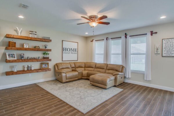 Cozy living room featuring a large sectional sofa, decorative wooden shelves with plants and decor, a "HOME sweet home" wall art, and natural light from multiple windows, highlighting a modern and inviting space in a Winter Garden home.