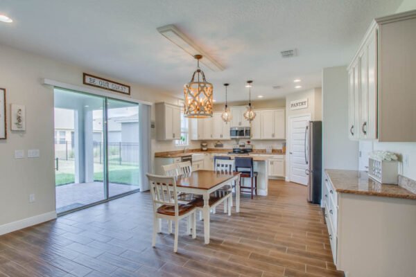 Modern kitchen interior with dining table, pendant lighting, and sliding glass door leading to fenced yard, featuring upgraded finishes and open floor plan, ideal for family living in Waterleigh community, Winter Garden.