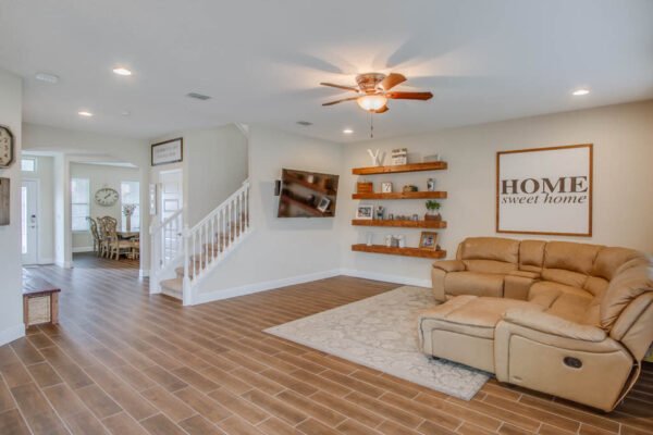 Spacious living room with modern decor, featuring a comfortable sectional sofa, wooden shelves displaying decor items, and a "HOME sweet home" wall art, showcasing the inviting interior of a property at 10175 Shallow Water Dr, Winter Garden, FL.