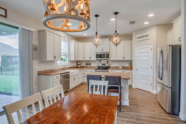 Modern kitchen interior featuring a large wooden dining table, white cabinetry, stainless steel appliances, and decorative pendant lighting, showcasing the upscale design of the Cresswell floor plan in Waterleigh community, Winter Garden, FL.