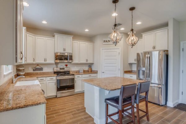 Modern kitchen with granite countertops, white cabinetry, stainless steel appliances, and pendant lighting, featuring an island with seating, located in a newly built home in the Waterleigh community, Winter Garden, FL.