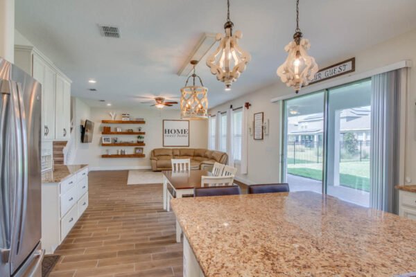 Modern kitchen and living area in a new home showcasing open floor plan, granite countertop, stylish lighting fixtures, and cozy seating, located in the desirable Waterleigh community of Winter Garden, FL.
