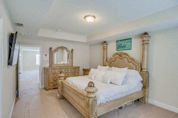 Spacious master bedroom featuring a luxurious wooden bed frame, plush bedding, and an elegant dresser, set in a modern home in the Waterleigh community of Winter Garden, FL.