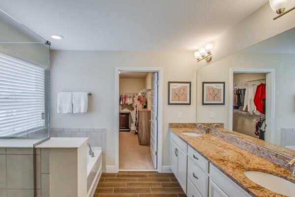 Spacious bathroom featuring dual sinks, granite countertops, and a soaking tub, with an adjacent walk-in closet and modern decor.