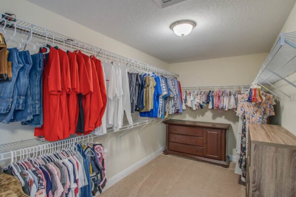 Walk-in closet featuring organized clothing racks with a variety of shirts and pants, and a wooden dresser, showcasing ample storage space in a modern home.