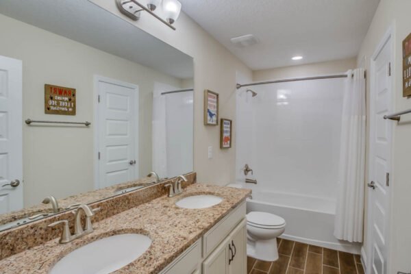 Modern bathroom featuring dual sinks with granite countertop, stylish fixtures, and a bathtub with shower, in a newly built home at 10175 Shallow Water Dr, Winter Garden, FL.