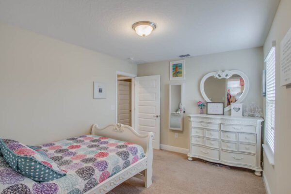 Bedroom featuring a white bed with colorful patterned bedding, a white dresser, a full-length mirror, and a light fixture, showcasing a cozy and inviting atmosphere in a modern home.