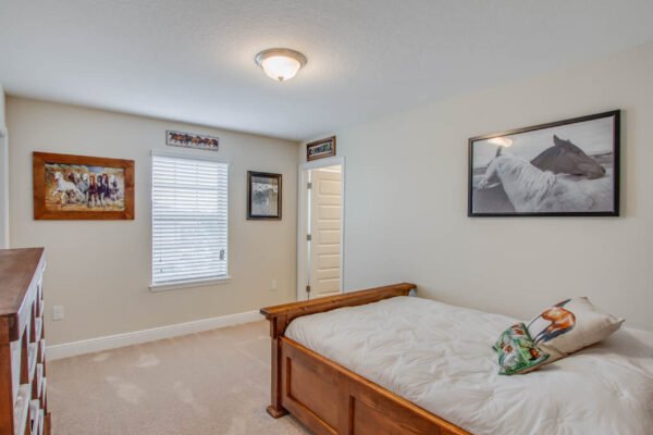 Cozy bedroom featuring a wooden bed with decorative pillow, framed horse artwork on walls, a window with blinds, and a light fixture, highlighting a modern and inviting atmosphere in a home.
