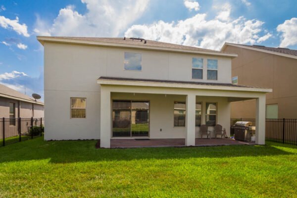 Back view of a modern two-story home in Winter Garden, Florida, featuring a covered patio, fenced backyard, and well-maintained lawn, highlighting the desirable Cresswell floor plan in the Waterleigh community.