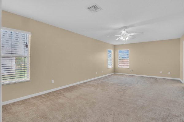Spacious interior of a four-bedroom home at 592 First Cape Coral Dr, Winter Garden, featuring light beige walls, carpeted flooring, and multiple windows allowing natural light.