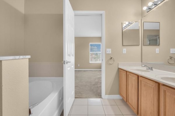Bathroom interior featuring a bathtub, double sink vanity with wooden cabinets, and large mirrors, showcasing an inviting and spacious design in a home at 592 First Cape Coral Dr, Winter Garden, FL.