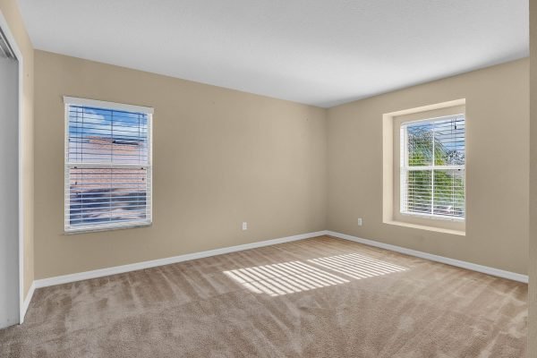Spacious, empty room with beige walls and large windows allowing natural light, showcasing potential for interior updates in a 4-bedroom home at 592 First Cape Coral Dr, Winter Garden, FL.