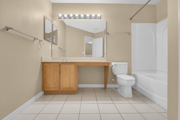 Spacious bathroom featuring a double vanity with mirrors, a toilet, and a bathtub, showcasing neutral tones and tiled flooring, ideal for the property at 592 First Cape Coral Dr, Winter Garden, FL.