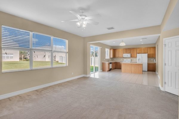 Spacious living area with carpet flooring, large windows for natural light, and an open kitchen featuring wooden cabinetry, located in a 4-bedroom home for sale at 592 First Cape Coral Dr, Winter Garden, FL.