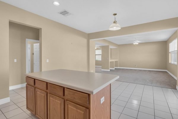 Open-concept living space featuring a kitchen island with wooden cabinetry, tile flooring, and natural light from windows, showcasing the potential for interior updating in a large 4-bedroom home at 592 First Cape Coral Dr, Winter Garden, FL.
