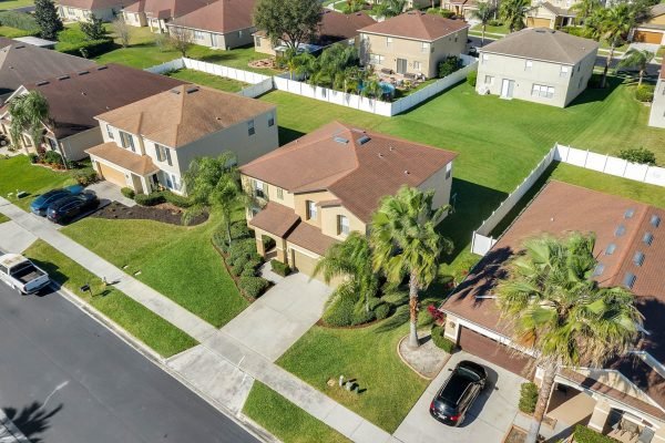 Aerial view of 592 First Cape Coral Dr in Winter Garden, FL, showcasing a spacious 4-bedroom home surrounded by green lawns and palm trees, located in a gated community with nearby amenities.