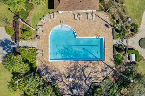 Aerial view of a community swimming pool with lounge chairs, surrounded by landscaped greenery, located in a gated community near 592 First Cape Coral Dr, Winter Garden, FL.