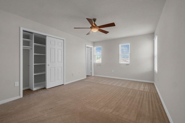 Spacious master bedroom with ceiling fan, natural light from windows, and closet space in pristine 4-bedroom home at 8073 Bowery Dr, Winter Garden, FL.