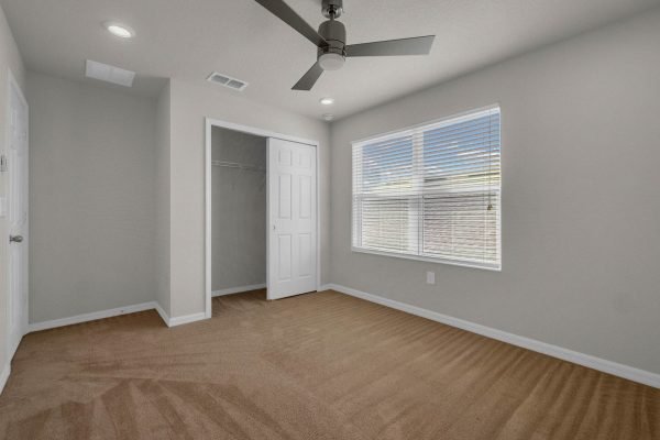 Spacious bedroom with carpeted floor, ceiling fan, and large window, featuring a closet and neutral-colored walls, ideal for a family home in Winter Garden.