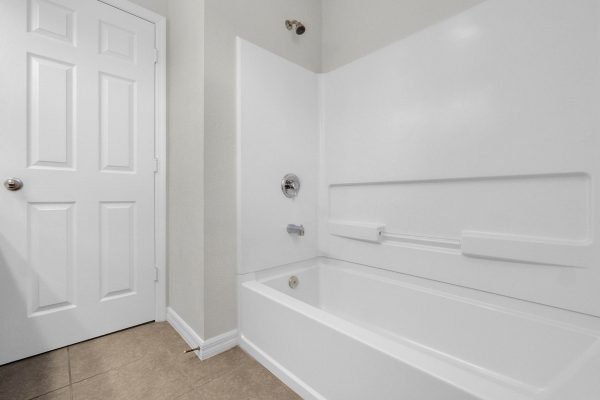 Clean and modern bathroom featuring a white bathtub with a shower fixture, beige tiled floor, and a closed door, highlighting the pristine condition of the home at 8073 Bowery Drive in Winter Garden, FL.