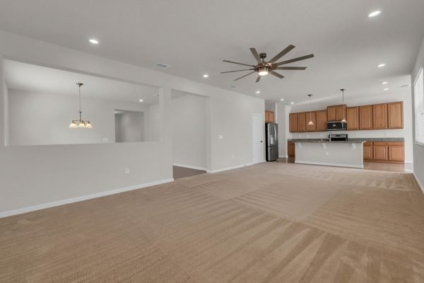 Spacious living area of 8073 Bowery Drive in Winter Garden, featuring an open floor plan, carpeted flooring, modern ceiling fan, and kitchen with wooden cabinets and stainless steel appliances.