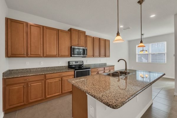 Modern kitchen in Winter Garden home featuring granite countertops, wooden cabinets, stainless steel appliances, and pendant lighting.