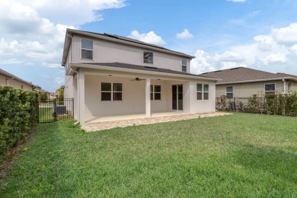 Backyard view of 8073 Bowery Drive in Winter Garden, FL, showcasing a spacious lawn, covered patio, and conservation area, emphasizing outdoor living space and tranquility.