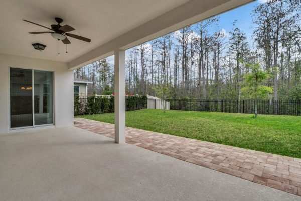 Covered patio overlooking a spacious, fully fenced backyard with conservation area and trees, showcasing the outdoor living space of a 4-bedroom home in Winter Garden, Florida.