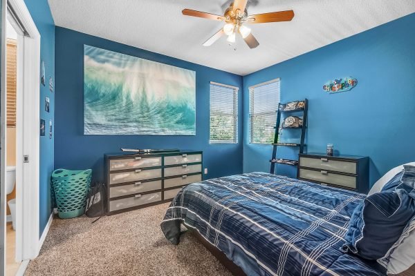 Bedroom featuring blue walls, a large wave painting, a plaid bedspread, and a dresser, showcasing a cozy and inviting atmosphere ideal for relaxation.