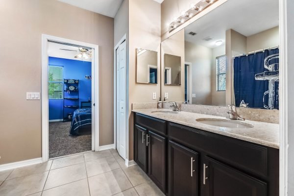 Bathroom with dual sinks, dark cabinetry, and large mirrors, leading to a blue-themed bedroom beyond, showcasing a bright and inviting interior.