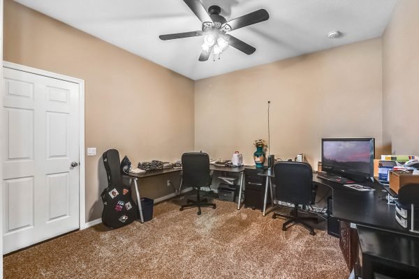 Home office with two desks, computer setup, and a guitar in a cozy, carpeted room.