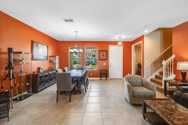 Interior view of a spacious living area in a home at 11717 Sheltering Pine Dr, featuring an orange accent wall, a dining table with chairs, elegant decor, and a staircase leading to the upper floor.