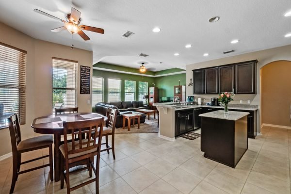 Open-concept kitchen and dining area in a modern Orlando home, featuring a dining table, dark cabinetry, and spacious living room with natural light.