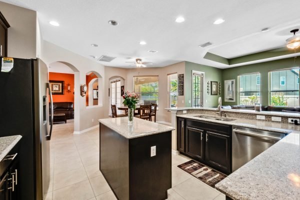 Modern kitchen with granite countertops, dark cabinetry, and open layout, showcasing dining area and natural light from windows, ideal for family gatherings in 11717 Sheltering Pine Dr, Orlando, FL.