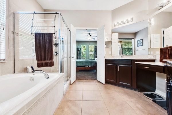 Spacious bathroom featuring a large soaking tub, glass shower, dark wood cabinetry, and natural light from windows, showcasing a modern design ideal for a luxury home in Orlando.