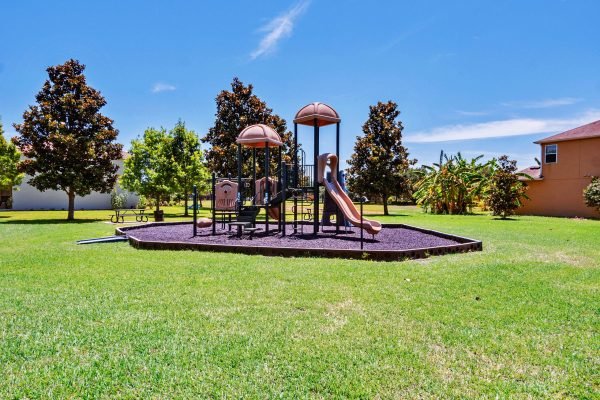 Playground equipment with slides and climbing structures in a grassy yard, surrounded by trees and residential homes, ideal for families in the Windermere area.