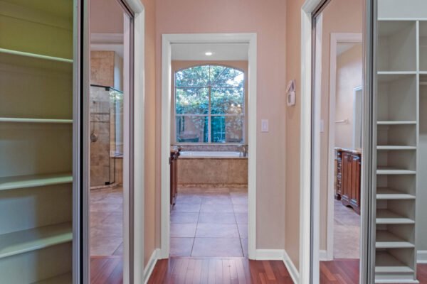 Interior hallway view showcasing a spacious layout with doorways leading to a luxurious bathroom and closet, featuring natural light from large windows and elegant wood flooring.