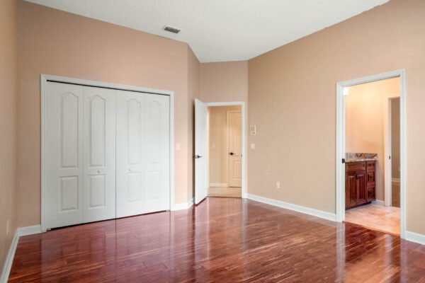 Spacious bedroom with hardwood flooring, double closet doors, and access to a bathroom in a custom home at 11359 Willow Gardens Drive, Windermere, FL.