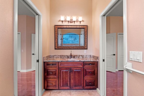 Elegant bathroom vanity area with dark wood cabinetry, granite countertop, and decorative mirror, featuring warm lighting and soft peach walls, showcasing a spacious layout typical of custom homes in Windermere, FL.