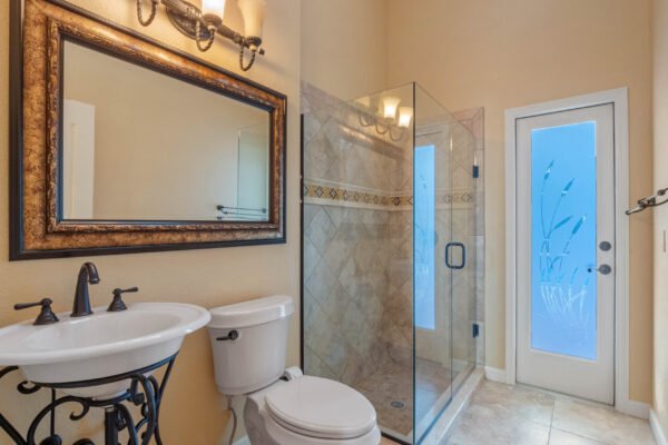 Elegant bathroom featuring a glass shower, decorative tile accents, a stylish framed mirror, and a modern sink with ornate fixtures, showcasing luxurious design elements in a custom home in Windermere, FL.