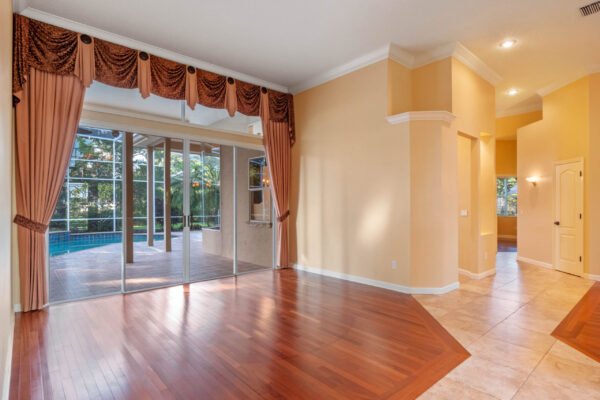 Elegant interior of a custom home in Windermere, featuring hardwood flooring, large windows with pool views, and decorative drapery, highlighting the spacious living area leading to outdoor living space.