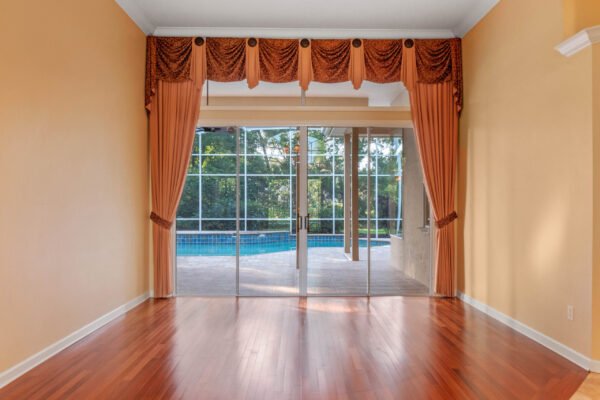 Elegant interior view showcasing large sliding glass doors leading to a pool area, framed by custom drapery, with polished hardwood floors and warm wall colors, emphasizing the luxurious design of the Windermere home at 11359 Willow Gardens Drive.