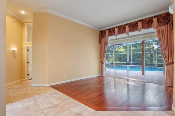 Spacious living area with wood flooring and large windows overlooking the pool, featuring elegant drapery and a seamless transition to outdoor living, in a custom home at 11359 Willow Gardens Drive, Windermere, FL.
