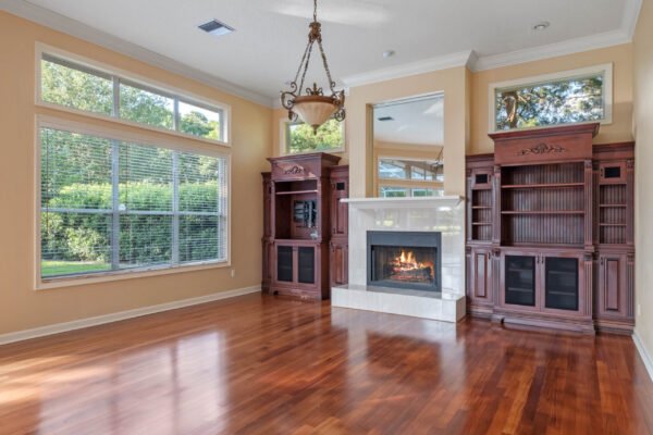 Elegant living room with large windows, hardwood flooring, and a cozy fireplace, showcasing custom cabinetry and natural light, reflecting the luxurious features of the Windermere home at 11359 Willow Gardens Drive.