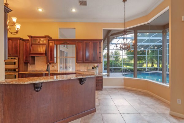 Elegant kitchen with dark wood cabinetry, granite countertops, and modern appliances, featuring large windows overlooking a screened-in pool area in a custom home in Windermere, Florida.