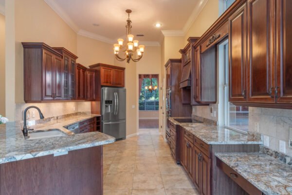 Elegant kitchen featuring dark wood cabinetry, granite countertops, stainless steel appliances, and a chandelier, showcasing a spacious layout in a custom home at 11359 Willow Gardens Drive, Windermere, FL.
