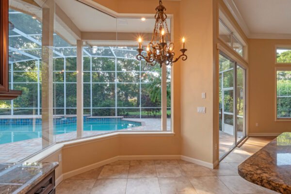 Elegant kitchen view showcasing a chandelier, large windows overlooking a screened-in pool area, and stylish granite countertops in a custom home at 11359 Willow Gardens Drive, Windermere, FL.