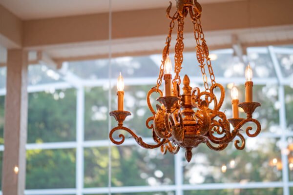 Elegant chandelier with ornate design and warm lighting, suspended in a sunlit room with large windows, enhancing the luxurious ambiance of the Windermere home.