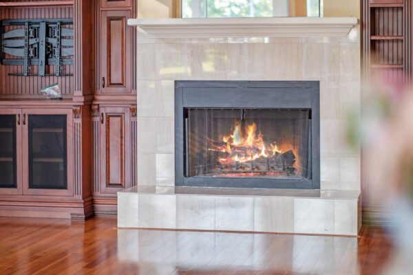 Cozy wood-burning fireplace with elegant stone surround and warm flames, set in a luxurious living space featuring rich wooden cabinetry and polished hardwood floors, ideal for the custom home at 11359 Willow Gardens Drive, Windermere, FL.